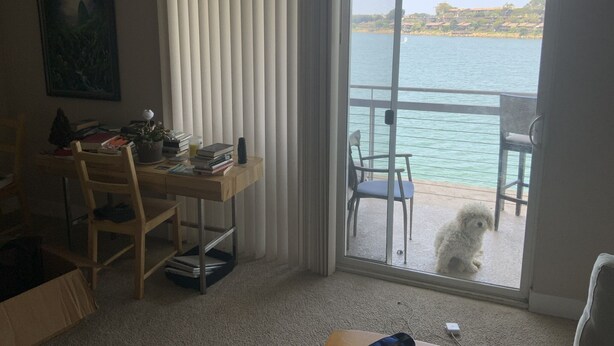 A room with a desk, chair, and a view of a body of water through a sliding door.