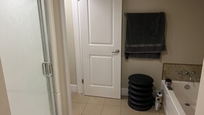 A bathroom with a white door, a towel rack, a stack of black circular stools, and a bathtub.