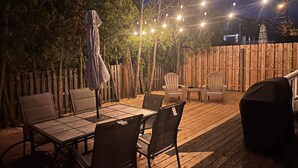 Eine Terrasse im Freien mit Holzboden, einem Tisch mit Stühlen, Lichterketten und einem Sonnenschirm.