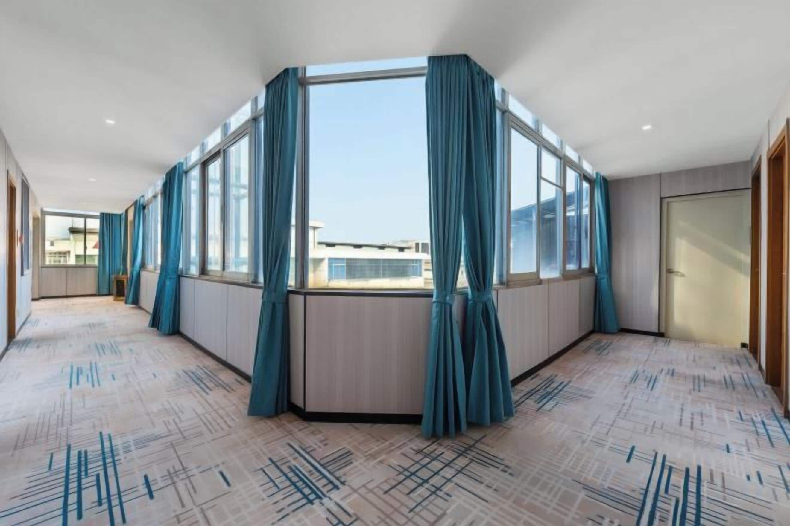 A hotel room with a large window, a corner view, and a patterned carpet.