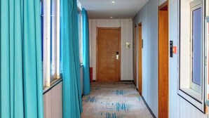 A hotel hallway with teal curtains, wooden doors, and patterned carpet. - Tianlong Boutique Hotel (Ji'an County)