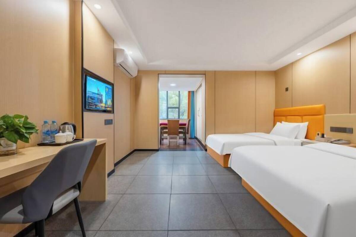 Een hotelkamer met een bureau, twee bedden, een televisie en uitzicht.