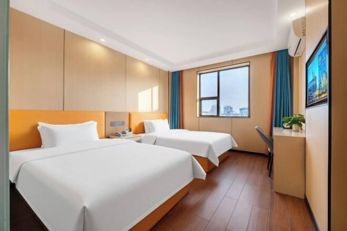 Hotelkamer met twee bedden, een bureau, een stoel, een raam met uitzicht op de stad, en een televisie aan de muur.