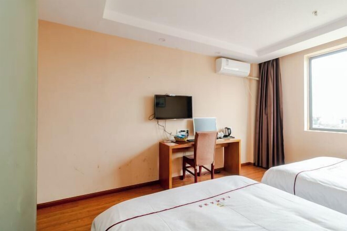 Habitación de hotel con dos camas, un escritorio con computadora y televisor, y una ventana con cortinas.