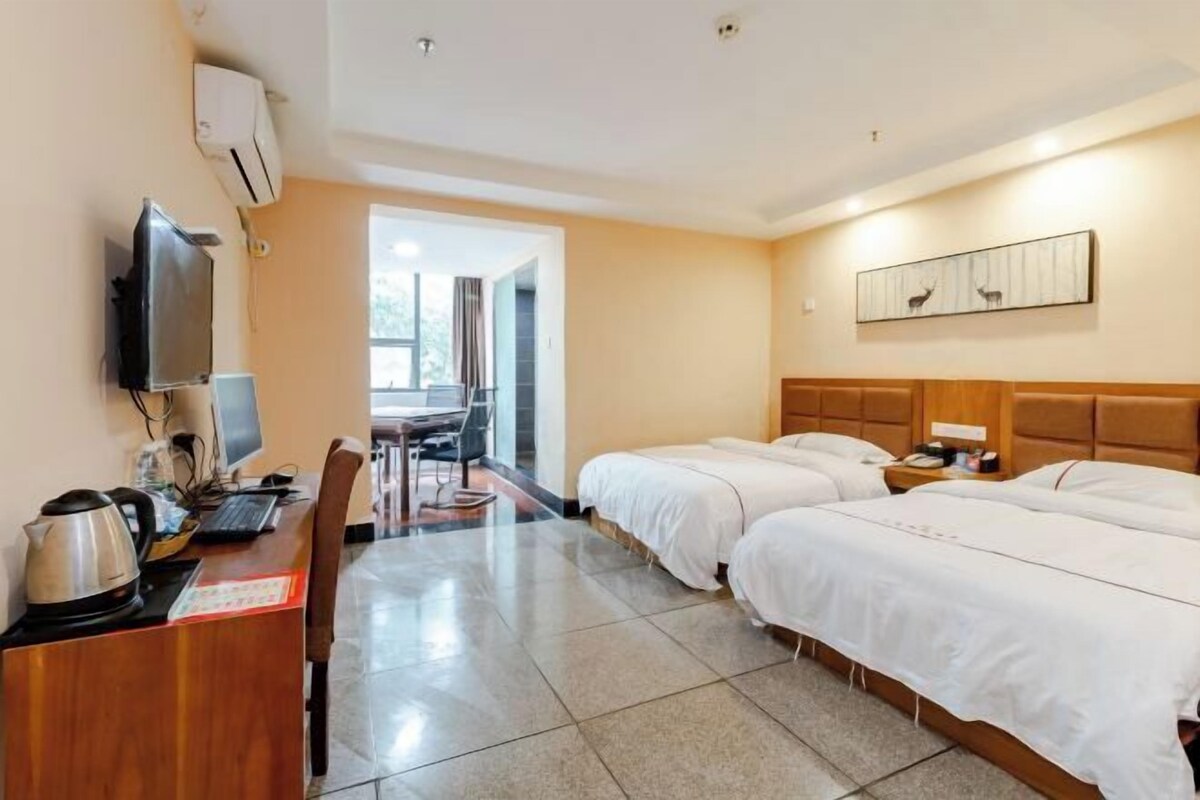 Habitación de hotel con dos camas, un escritorio con computadora y hervidor, televisor y un cuadro en la pared.
