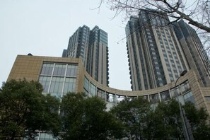 A high-rise building with a curved glass facade, surrounded by trees.
