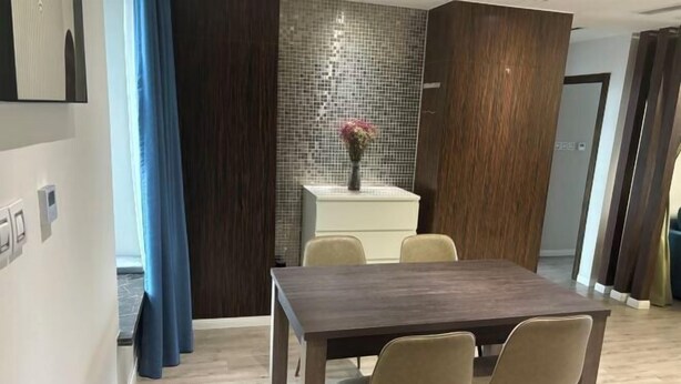 A modern dining area with a dark wooden table and beige chairs, a white cabinet with a vase of flowers, and a tiled backsplash. - Riyueguang Apartment Hotel (Shanghai)