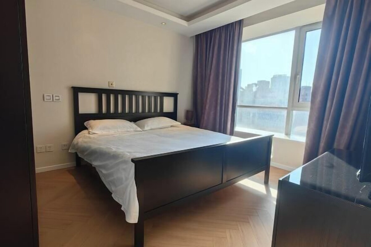A modern hotel room with a large bed, a desk, and a view of the city.
