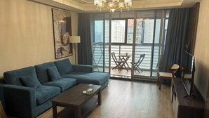 A modern living room with a sofa, coffee table, and a TV stand. There is a balcony with a table and chairs. - Riyueguang Apartment Hotel (Shanghai)