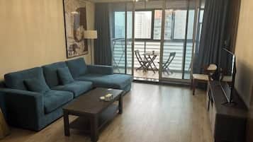 Una sala de estar moderna con un sofá, una mesa de centro y un mueble para televisión. Hay un balcón con una mesa y sillas.