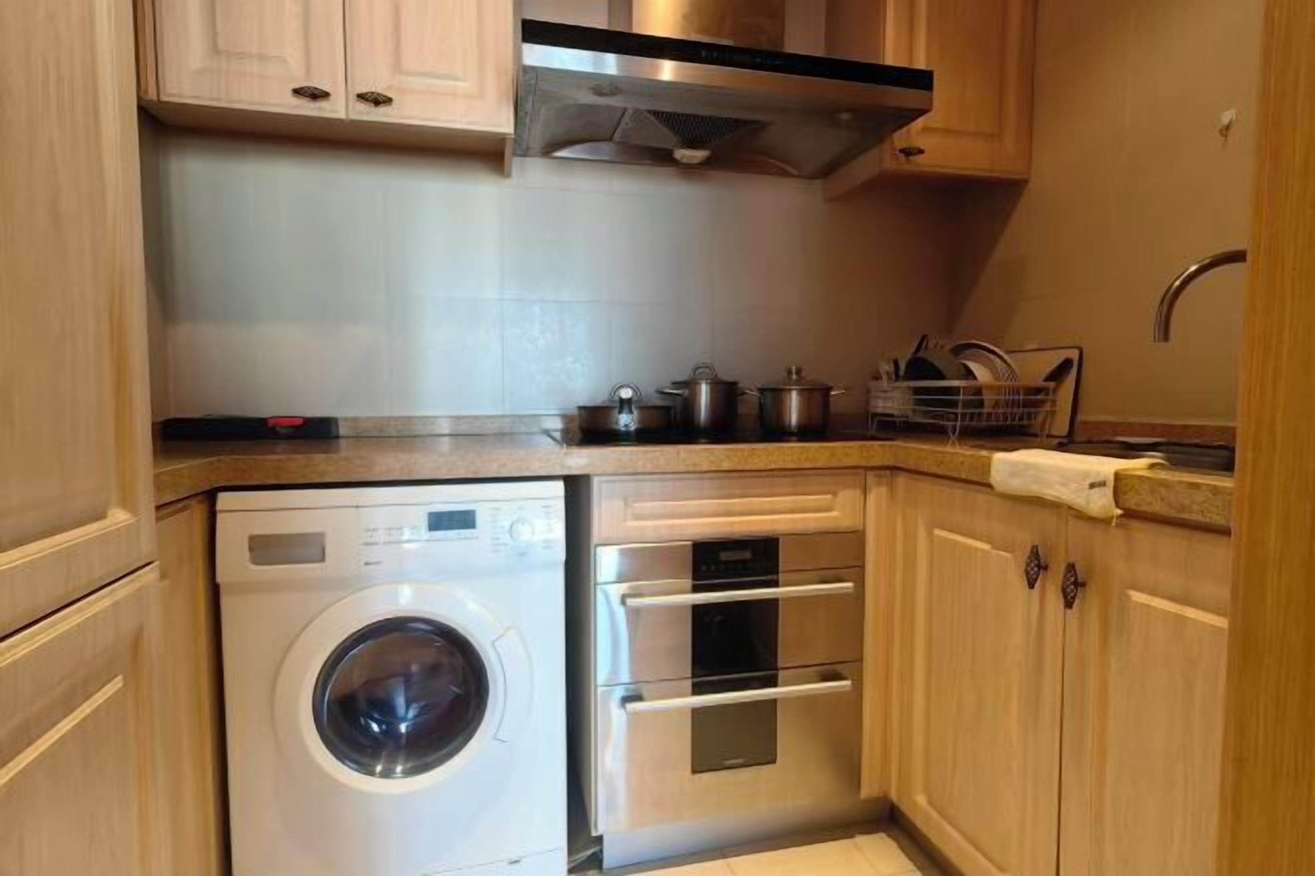 A compact kitchen with a built-in washer and oven, wooden cabinets, and a stainless steel range hood.