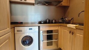 A compact kitchen with a built-in washer and oven, wooden cabinets, and a stainless steel range hood. - Riyueguang Apartment Hotel (Shanghai)