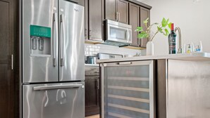 Un refrigerador de acero inoxidable con dispensador de agua, un microondas y una botella de vino sobre la encimera.