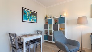 A dining area with a white table, grey chairs, a blue armchair, and a floor lamp. - Casa Encantada - Communal pool & garden, just a 5 minute walk to town centre (Carvoeiro)