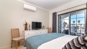 A bedroom with a bed, a TV on a dresser, a chair, and a large window with a view of buildings and palm trees. - Casa Encantada - Communal pool & garden, just a 5 minute walk to town centre (Carvoeiro)