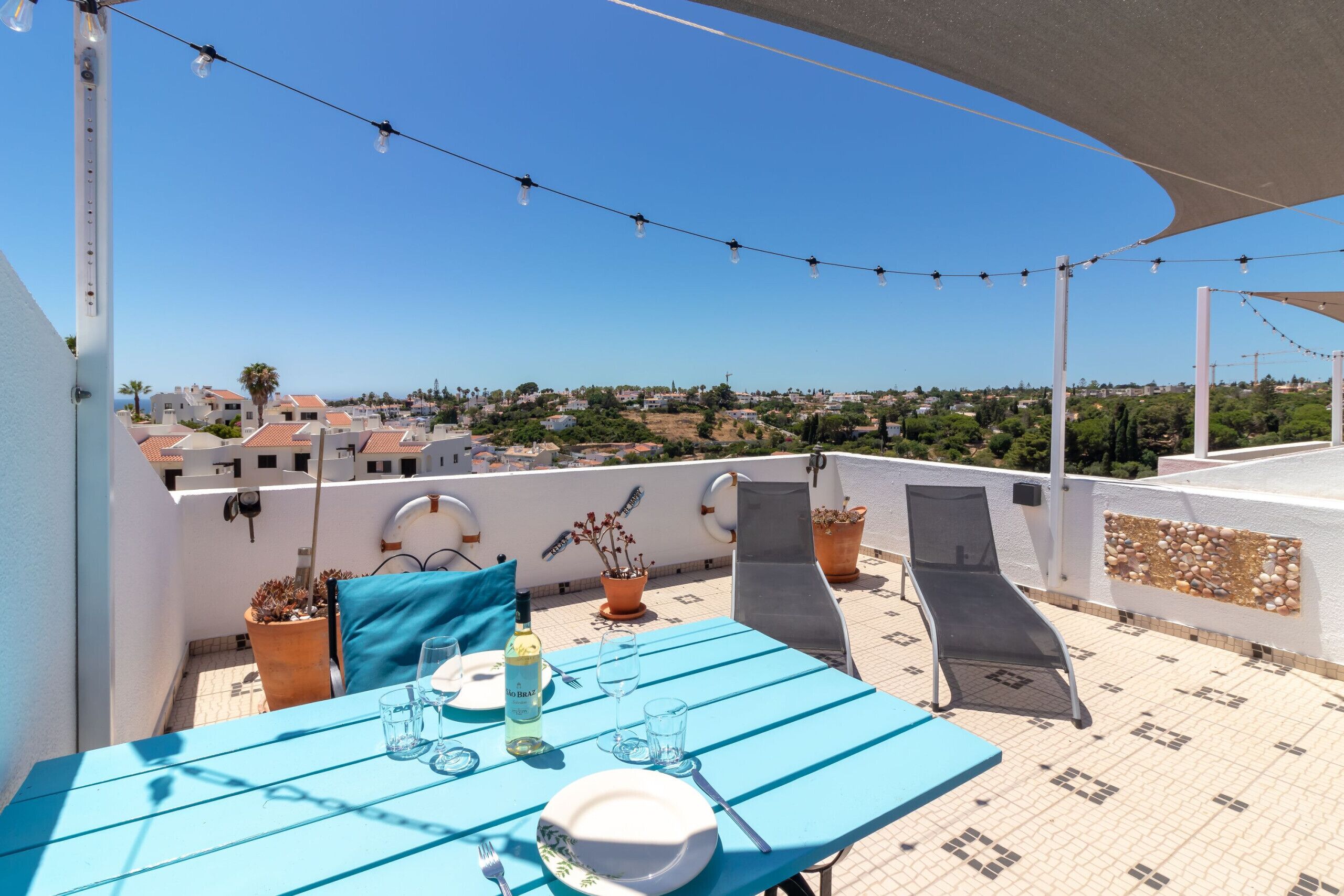 A rooftop terrace with a table set for two, potted plants, and a clear view of the cityscape.