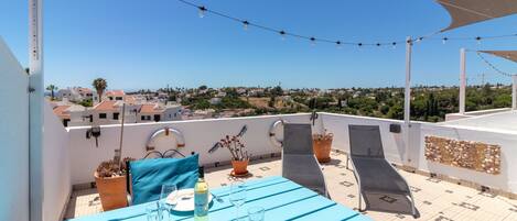 A rooftop terrace with a table set for two, potted plants, and a clear view of the cityscape.
