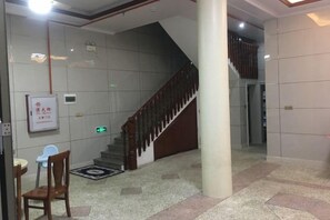 Un hall d’entrée avec un escalier, un comptoir de réception et un panneau sur le mur.
