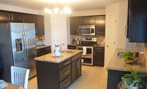 A modern kitchen with dark cabinetry, stainless steel appliances, granite countertops, and a central island with a sink. - POOL HOME - SUN & BEACH-5-BED 3-BATH-COME RELAX AND ENJOY PALM COAST !!! (Palm Coast)