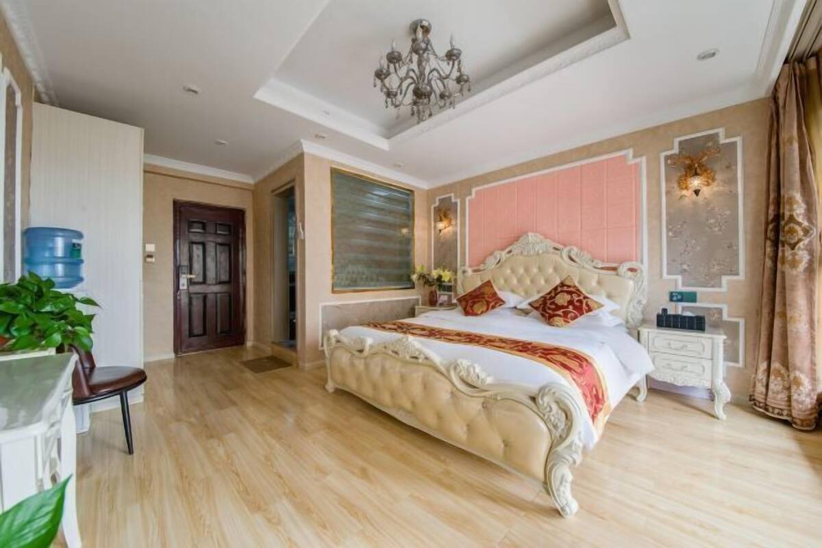 Een ruime slaapkamer met een groot bed, een kroonluchter en een moderne badkamer met een grote spiegel.