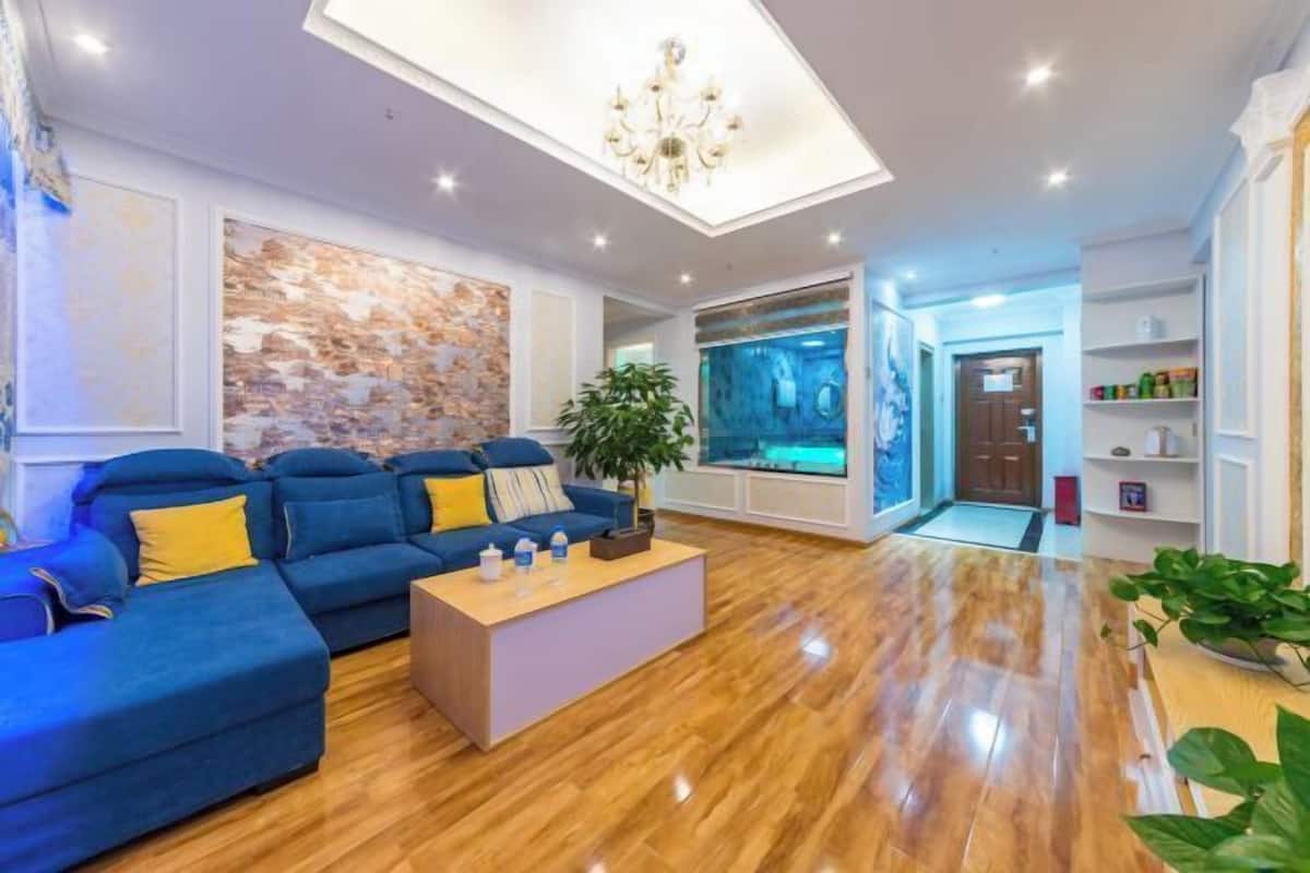 Een moderne woonkamer met een blauwe zithoek, een houten salontafel, een kroonluchter en een stenen wand.