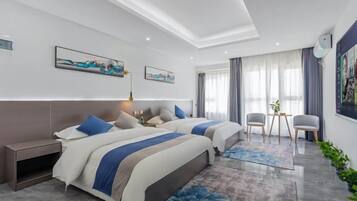 A hotel room with two beds, a desk, chairs, artwork on the walls, and a large window with curtains.
