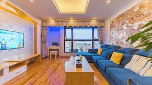 A modern living room with a sofa, coffee table, TV, and a view of the city through large windows.