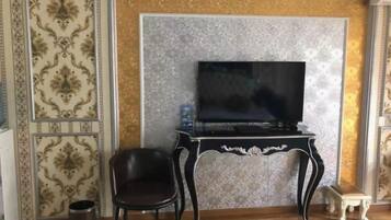 A room with a television on a black stand, a black chair, a small white table, and a patterned wall.