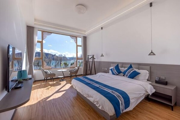Ett modernt hotellrum med en stor säng, ett skrivbord med en dator, en stol, ett litet bord och utsikt över bergen.