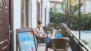 A covered outdoor seating area with wicker chairs and a table, a signboard with text, and a door with intricate woodwork. - Dali Qihai Station (Dali City)