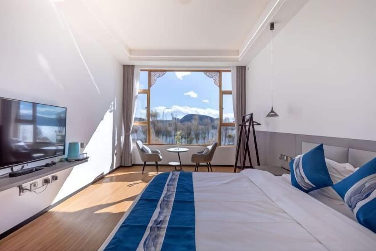 A hotel room with a bed, a TV, a desk, and a view of the outdoors.