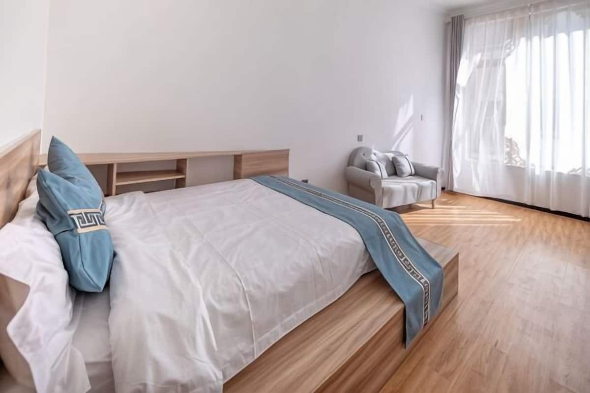 A bedroom with a bed, a chair, a desk, and a window with curtains.
