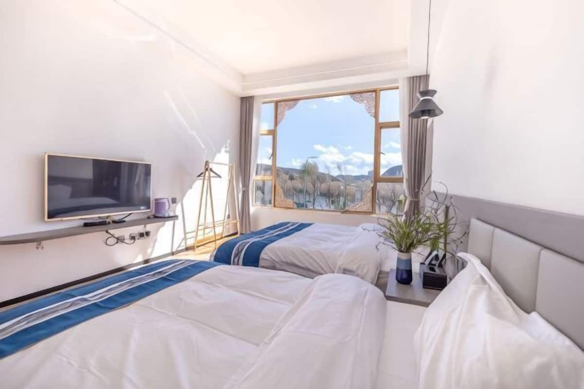 A hotel room with two beds, a TV, a window with a mountain view, and a plant on the nightstand.