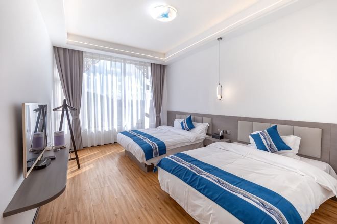 A hotel room with two beds, a desk, and a large window with curtains.