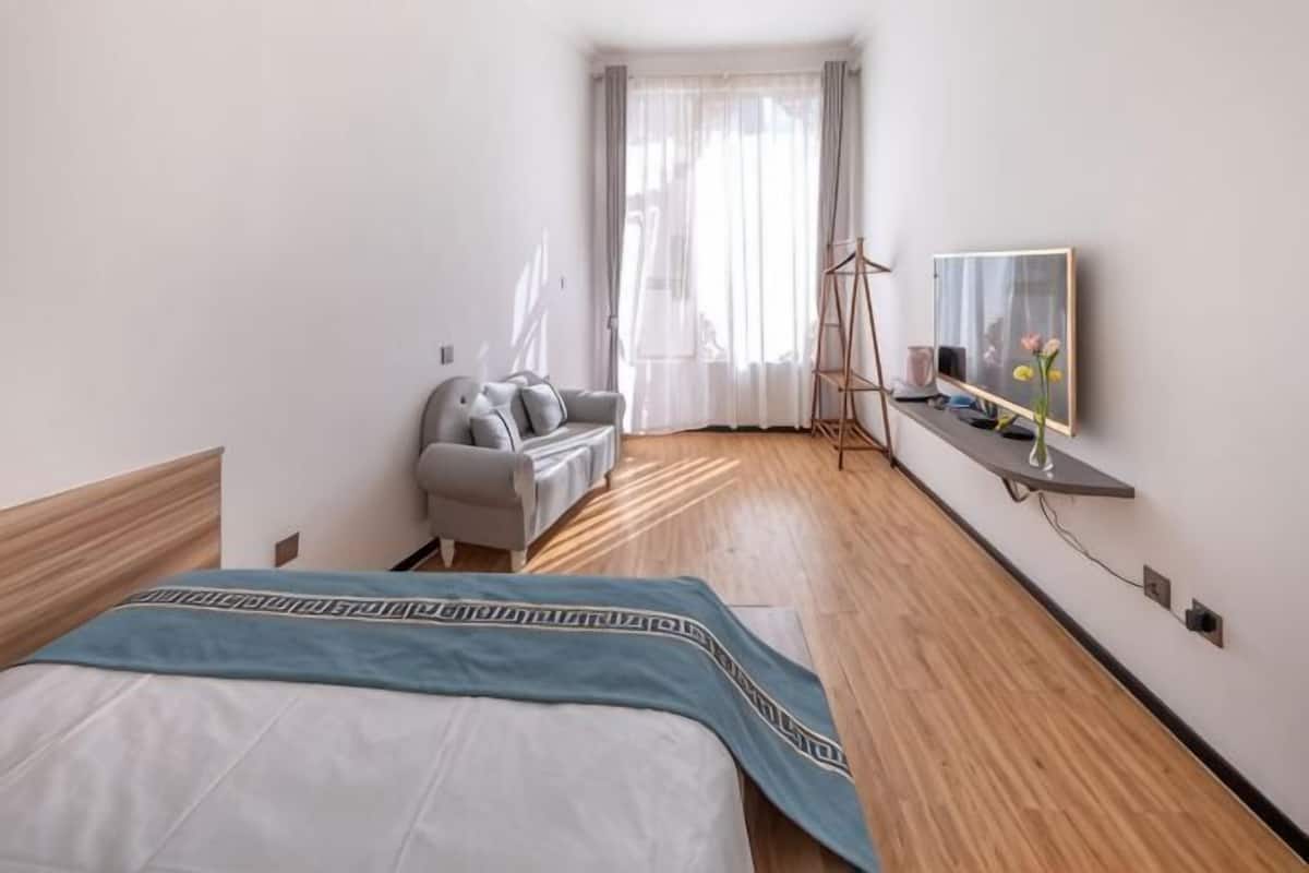 A hotel room with a bed, a sofa, a TV, and a window with curtains.