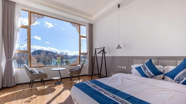 A hotel room with a large bed, a view of mountains, a small table, and two chairs. - Dali Qihai Station (Dali City)