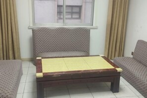 A room with a patterned sofa, a wooden table with a yellow top, and a window with curtains. - Guanyuntianyuebingguan (Guanyun)