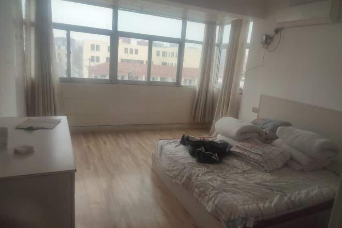 A bedroom with a bed, a desk, and a window with a view of buildings.