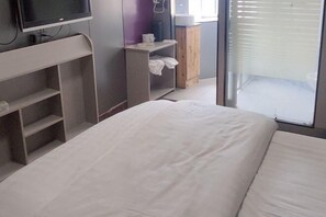 Une chambre d’hôtel avec un lit, un téléviseur posé sur un meuble, une armoire et une fenêtre avec des stores.