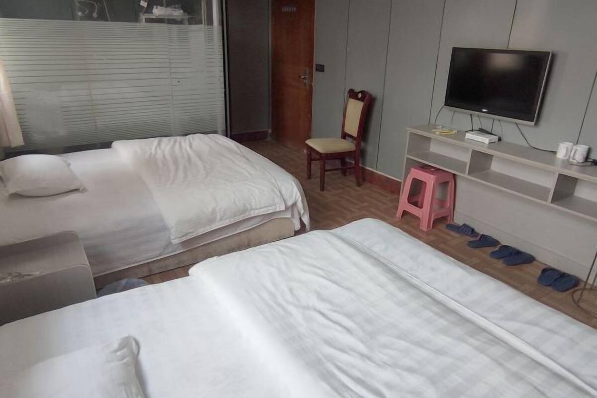 A hotel room with two beds, a television on a stand, a chair, and a small stool.