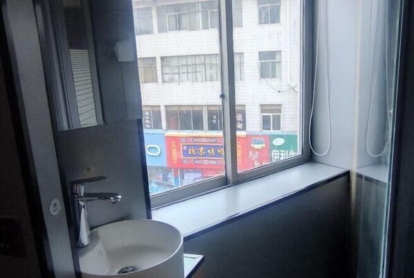 Un baño con lavamanos, una ventana y vistas a un edificio con señalización.