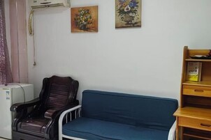 Um quarto com um sofá azul, uma cadeira de madeira e duas pinturas na parede.