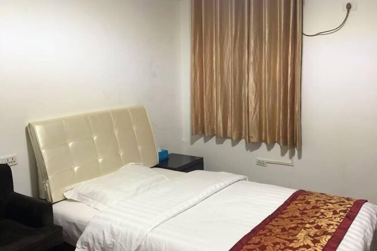 A hotel room with a bed, a nightstand, a chair, and a curtain.