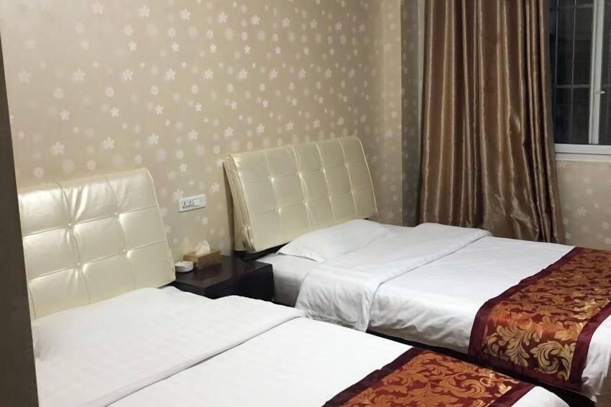 A hotel room with two beds, a nightstand, and a window with curtains.