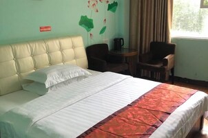 A hotel room with a bed, two chairs, a small table with a coffee pot, and a window with curtains.
