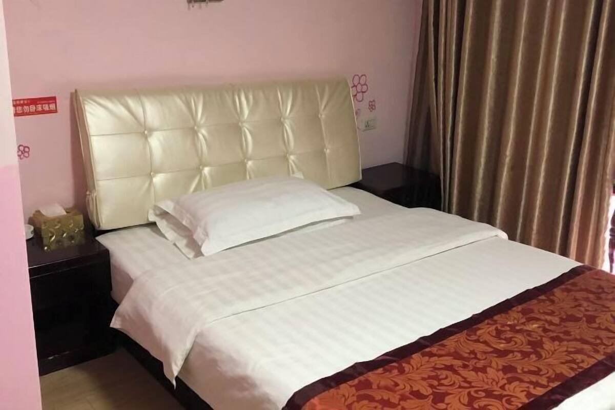 A hotel room with a bed, a nightstand, a decorative pillow, and a curtain.