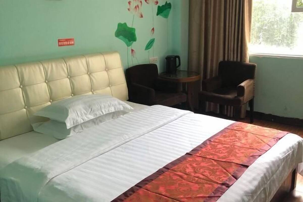 A hotel room with a bed, two chairs, a small table, and a window with curtains.