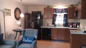 A living room with a sofa, a coffee table, and a ceiling fan. There is a kitchen area with cabinets and appliances.