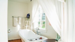 A bathroom with a freestanding bathtub, a white sink, and a window with sheer curtains. - Tuhitarata Hideaway. Romantic Couples Retreat (Pirinoa)