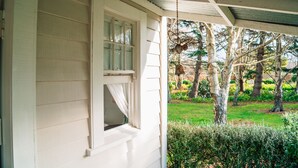 A covered porch with a window and a hanging bird feeder. - Tuhitarata Hideaway. Romantic Couples Retreat (Pirinoa)
